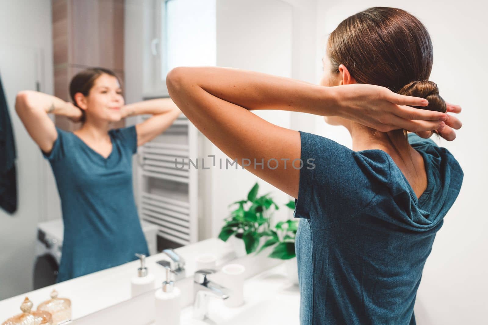 Back view of young woman standing in front of the mirror in the bathroom getting ready for sleep waring her night gown by VisualProductions