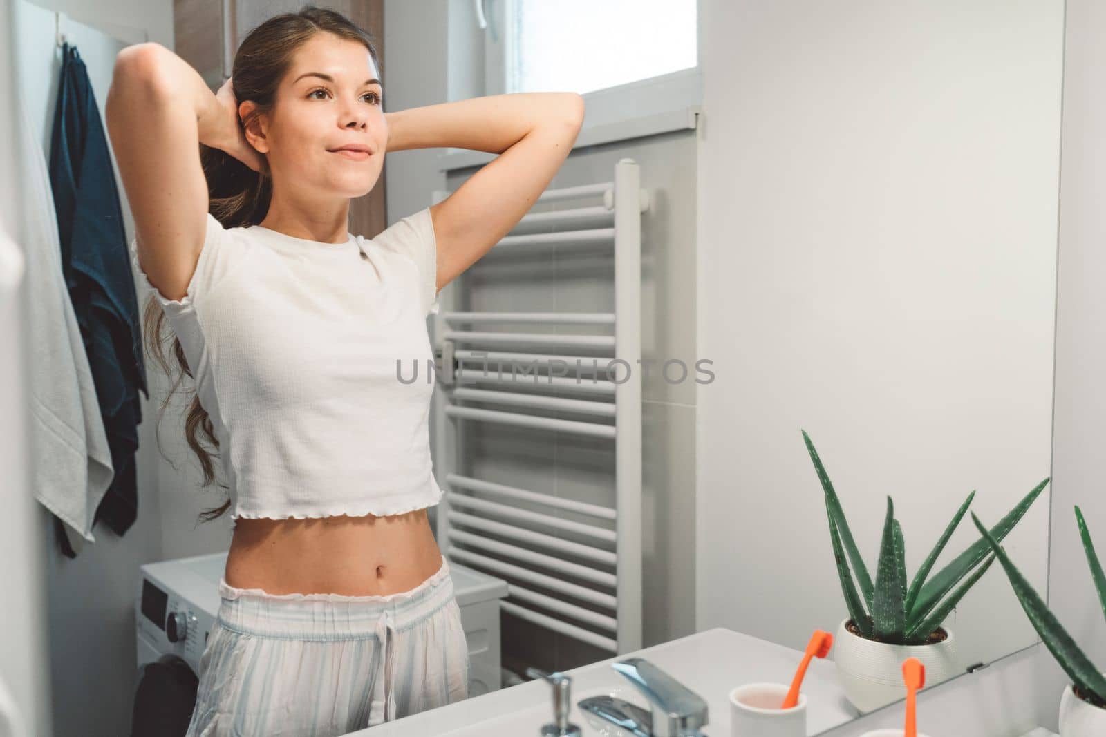 Young caucasian woman getting ready in a bright white modern bathroom. Woman doing her skincare, cleaning her face, teeth and body int he bathroom.