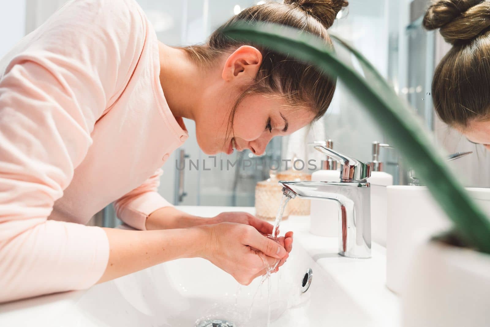 Side view of a woman washing her face in the sink in the morning when she wakes up by VisualProductions