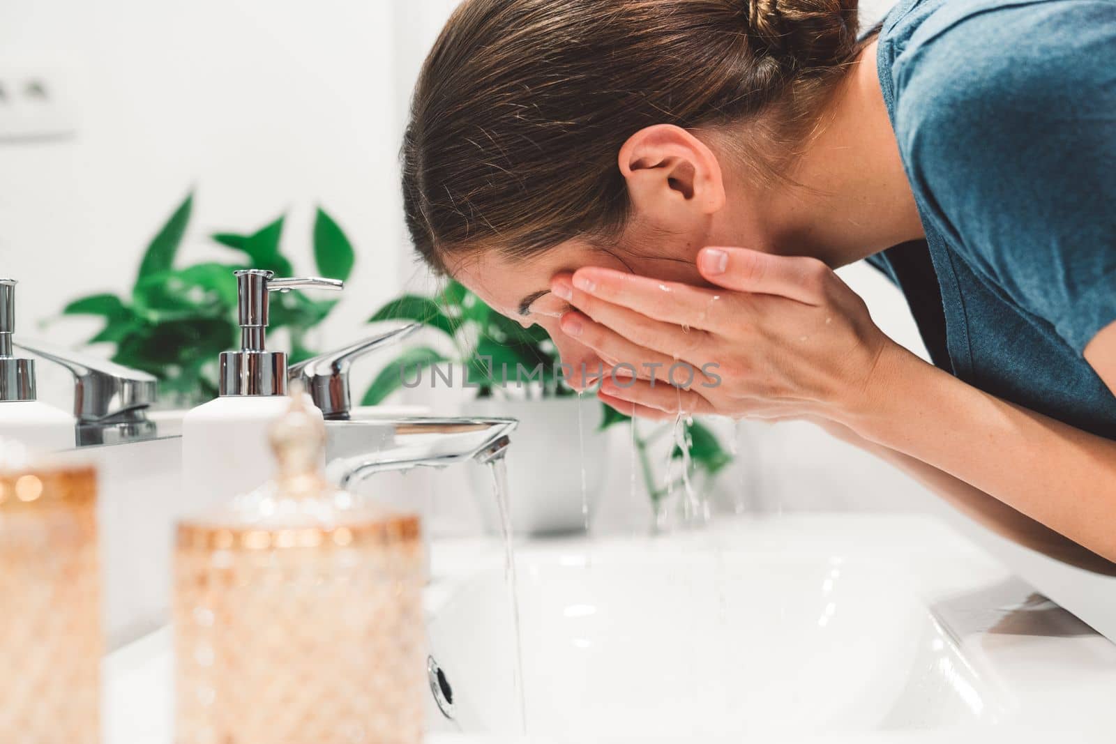 Young caucasian woman getting ready in a bright white modern bathroom. Woman doing her skincare, cleaning her face, teeth and body int he bathroom.