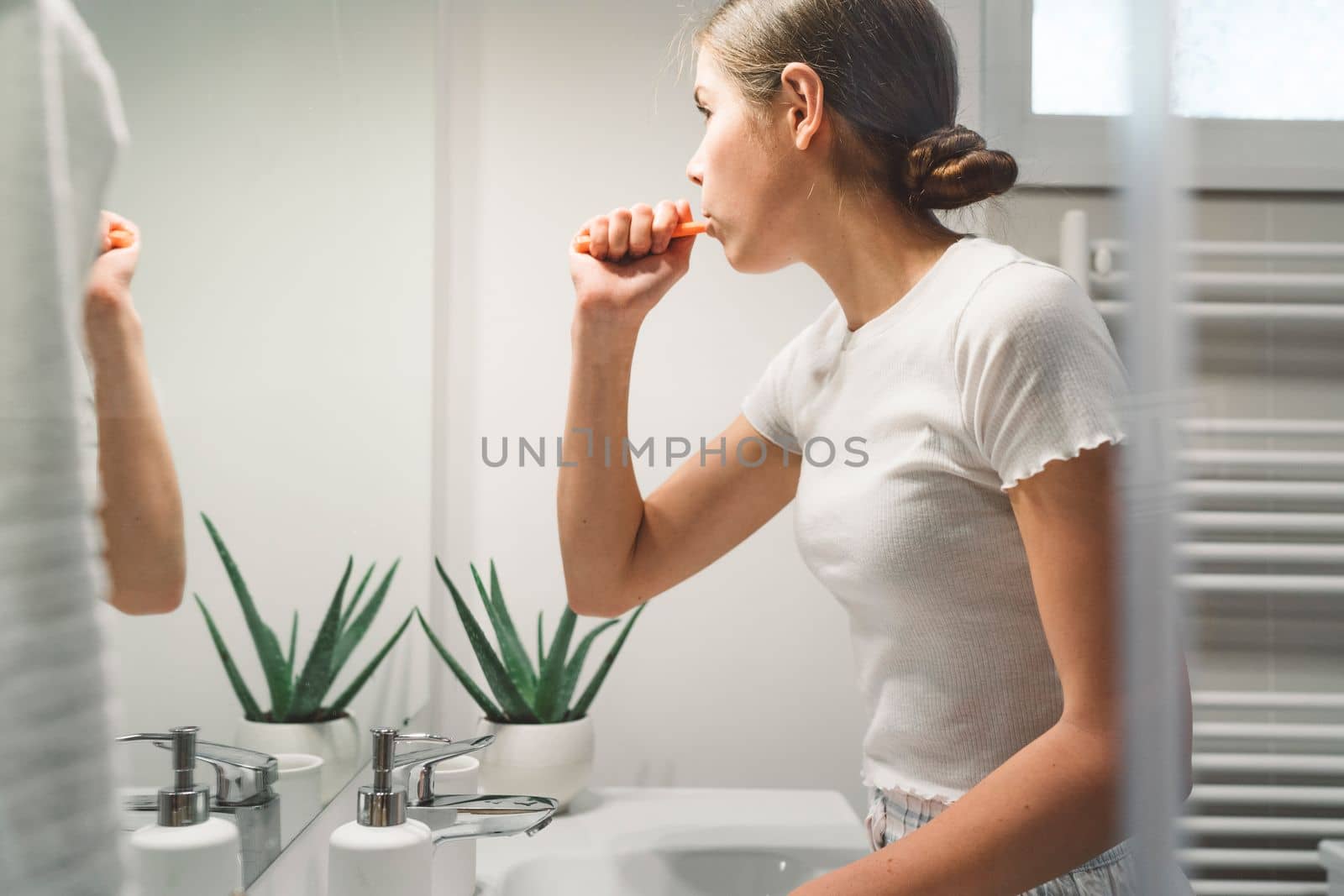 Young caucasian woman getting ready in a bright white modern bathroom. Woman doing her skincare, cleaning her face, teeth and body int he bathroom.