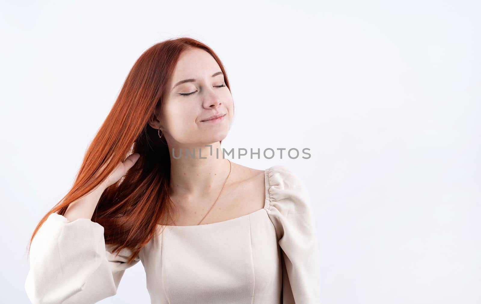 Happy beautiful woman smiling with closed eyes touching her red straight hair over white background, copy space