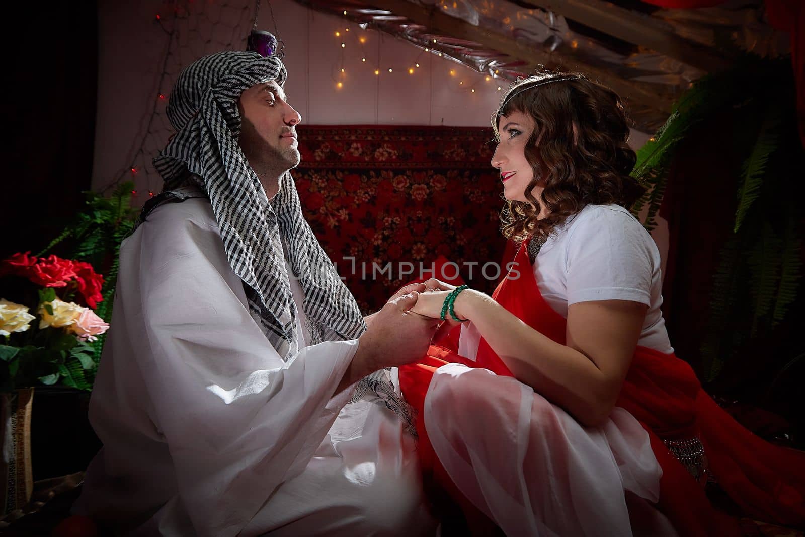 Portrait of young arabian muslim couple in traditional clothes in cozy red room. Fhoto shoot in easten style with male and female model like in harem with a sultan and an odalisque