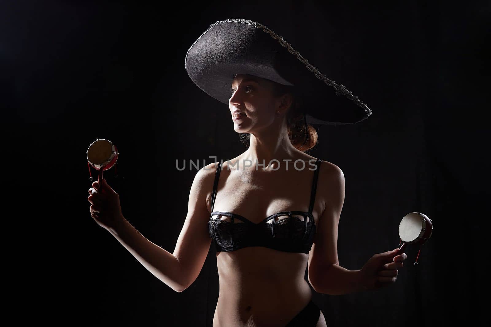 Silhouette of a beautiful young girl in black underwear and a Mexican hat on a dark background. Exotic model posing naked in the studio. Body portrait of sexy girl by keleny