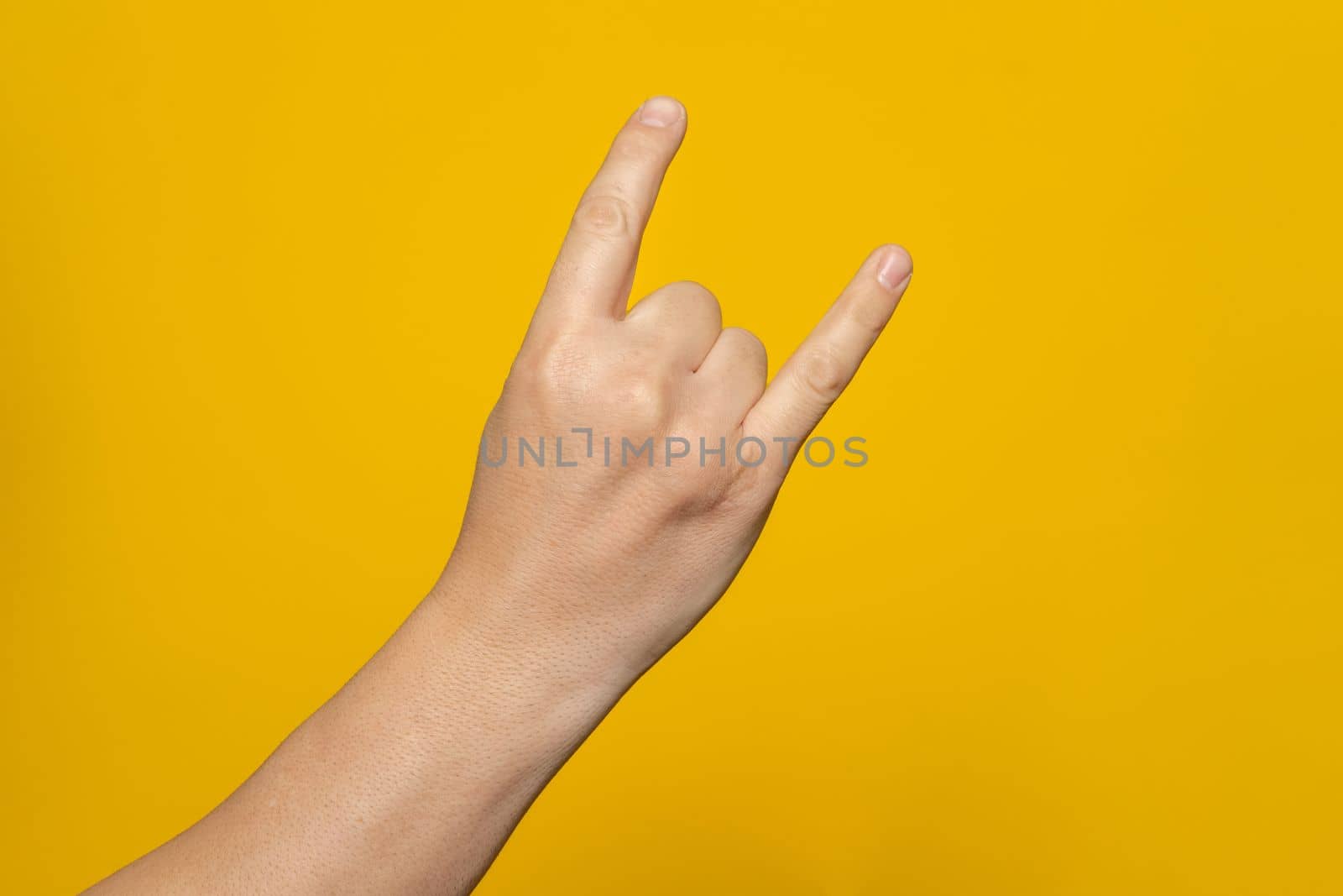 Male hand close-up on a yellow background shows hand gesture. Rock'n'roll. Isolate.