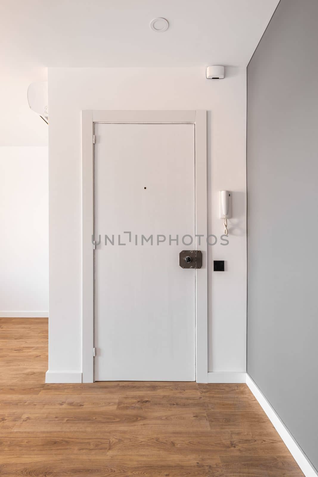 Entrance closed white wooden door to the apartment. Next to the door on the wall there is an intercom handset to allow guests to enter the entrance. On the door there is a key lock. by apavlin