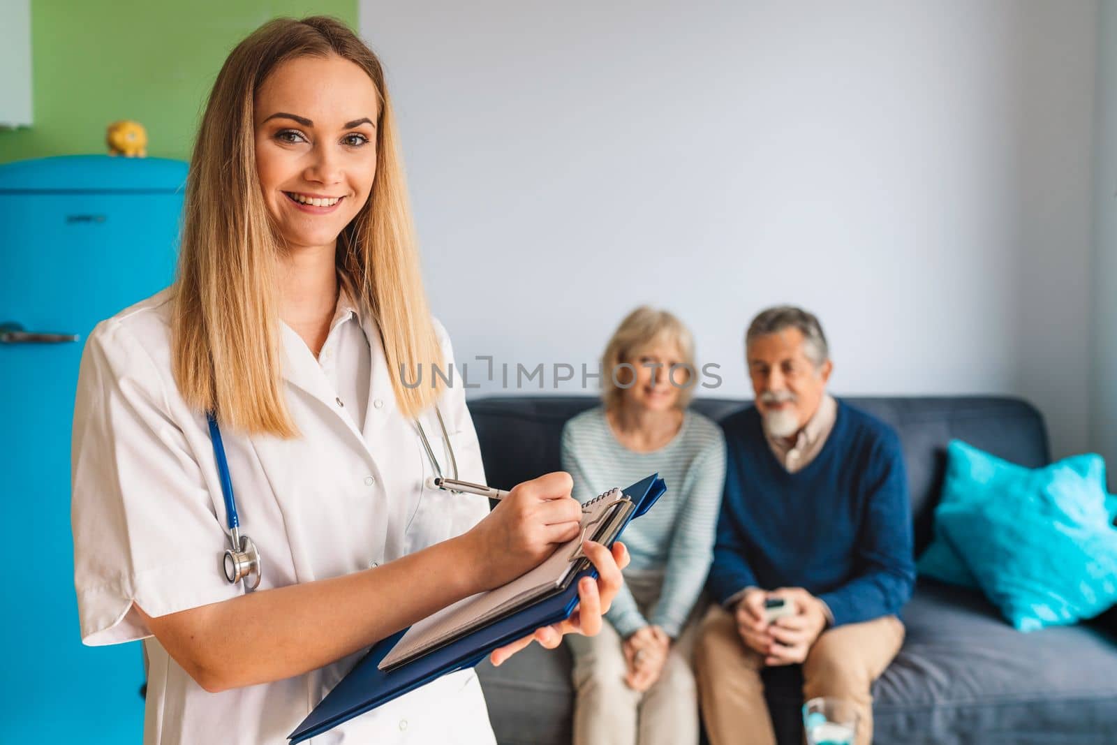 Young blonde woman caregiver helping senior married couple at home. Nurse assisting her senior patients at nursing home. Senior couple being helped by nurse at home. High quality photo