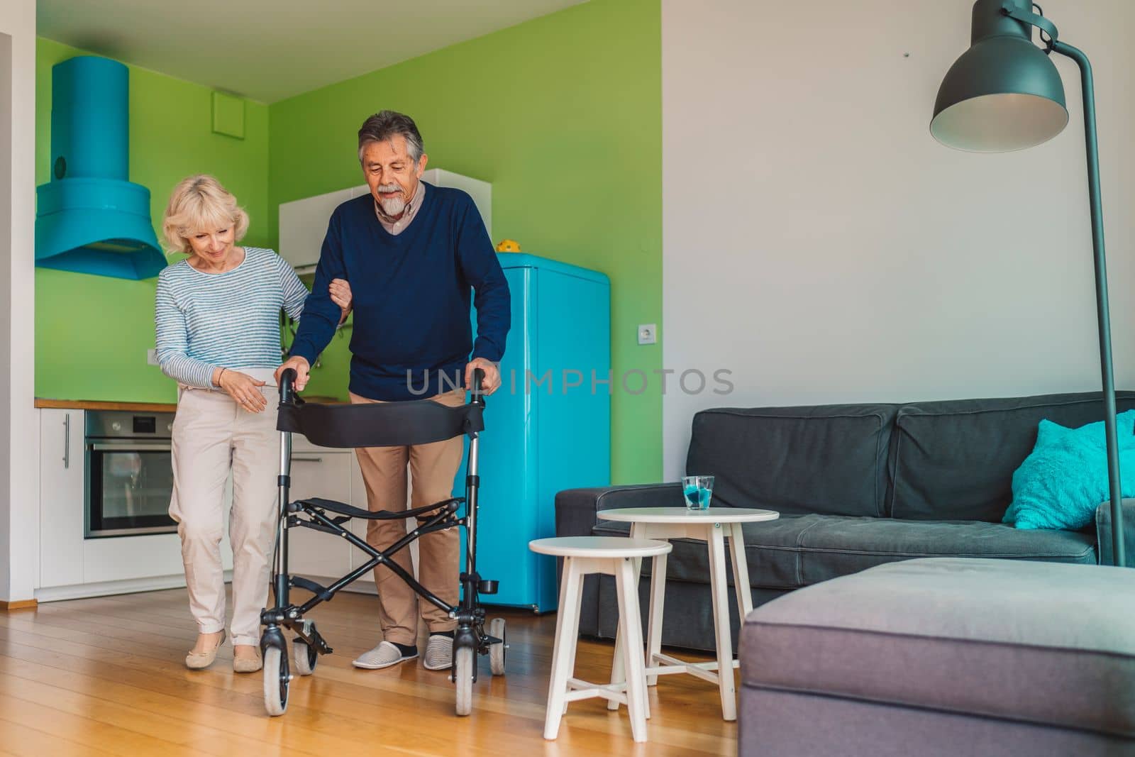 Senior woman helping senior man walking inside the apartment at home. High quality photo