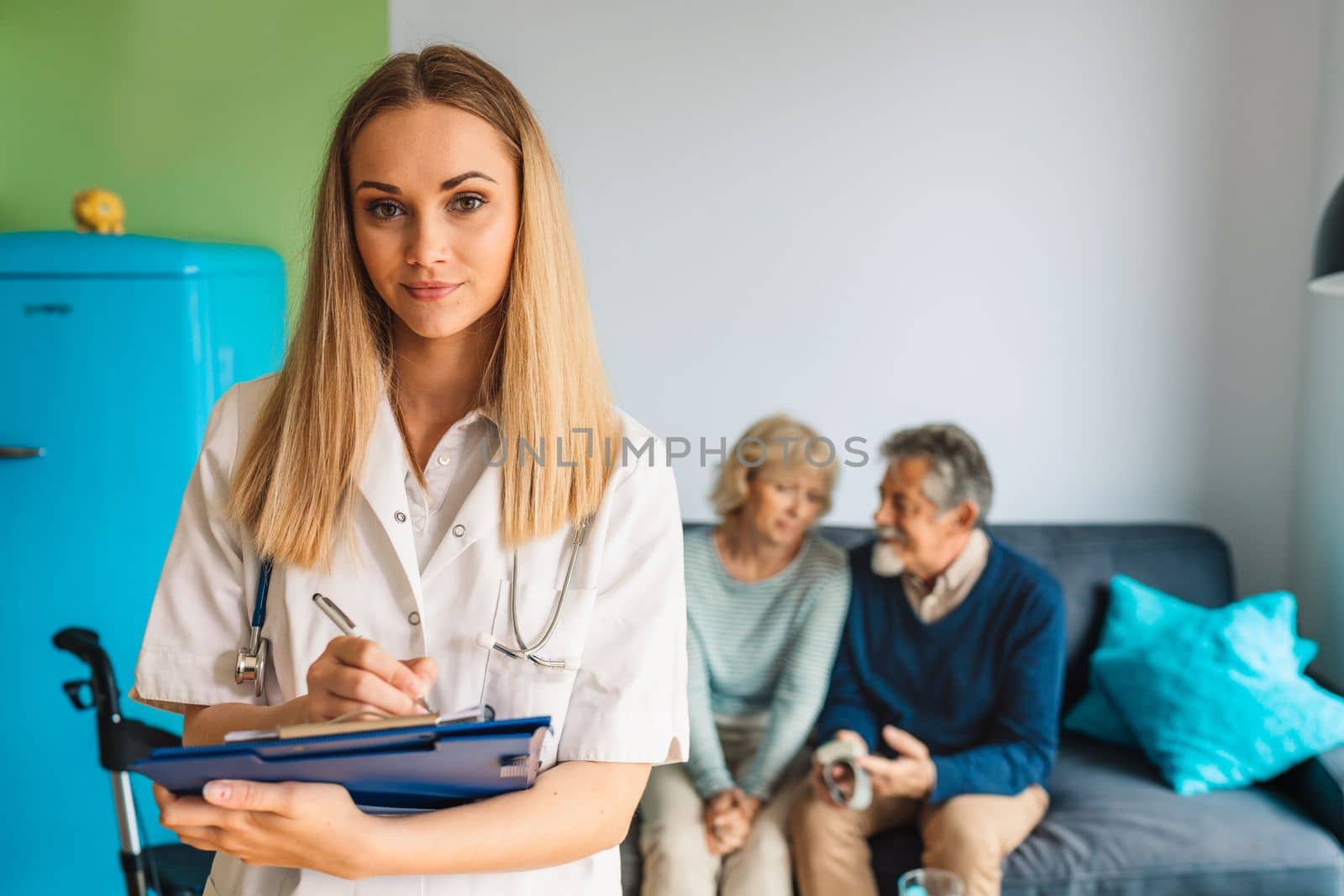 Young blonde woman caregiver helping senior married couple at home. Nurse assisting her senior patients at nursing home. Senior couple being helped by nurse at home. High quality photo