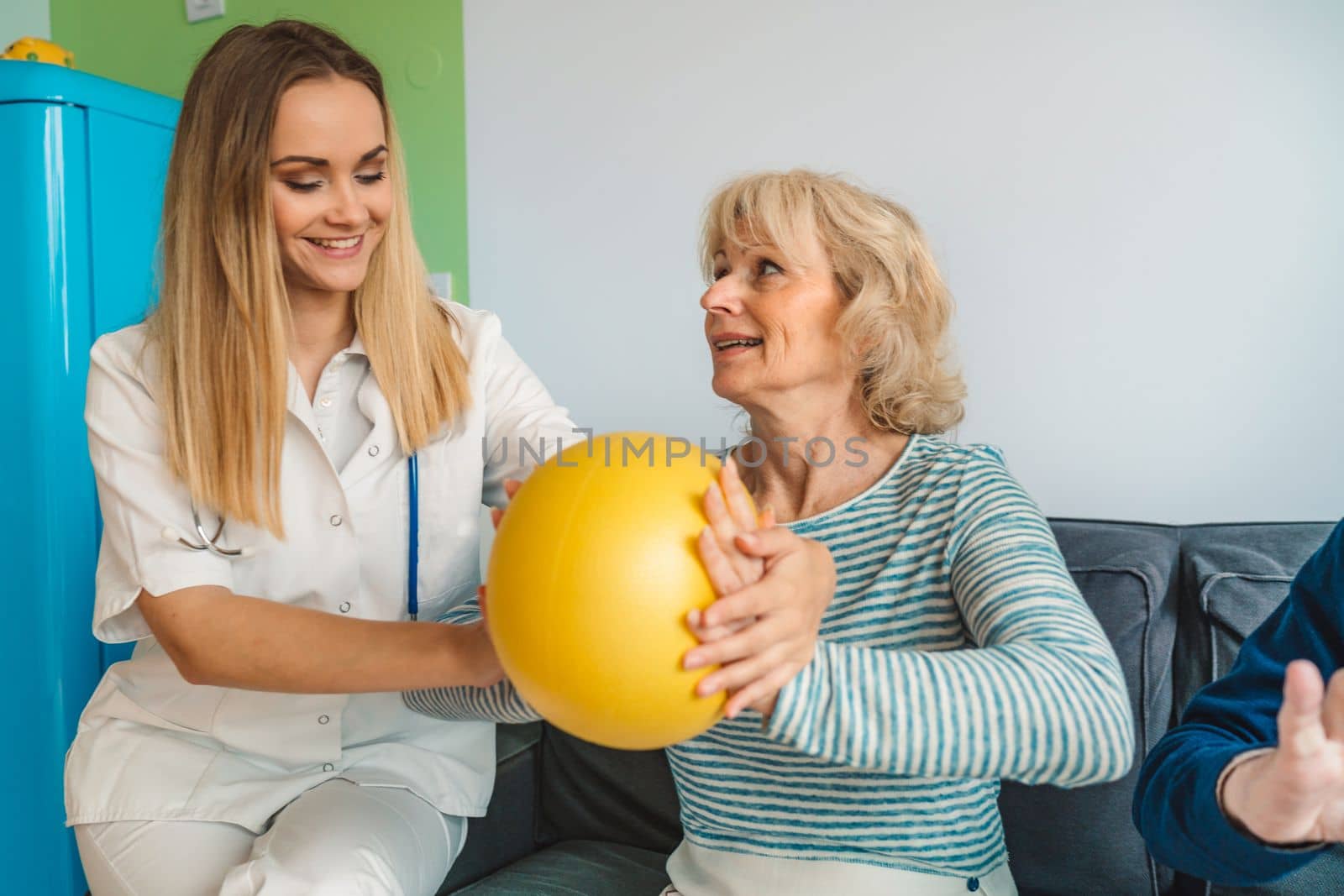 Young woman physiotherapist showing senior woman an exercise with yellow pilates ball by VisualProductions