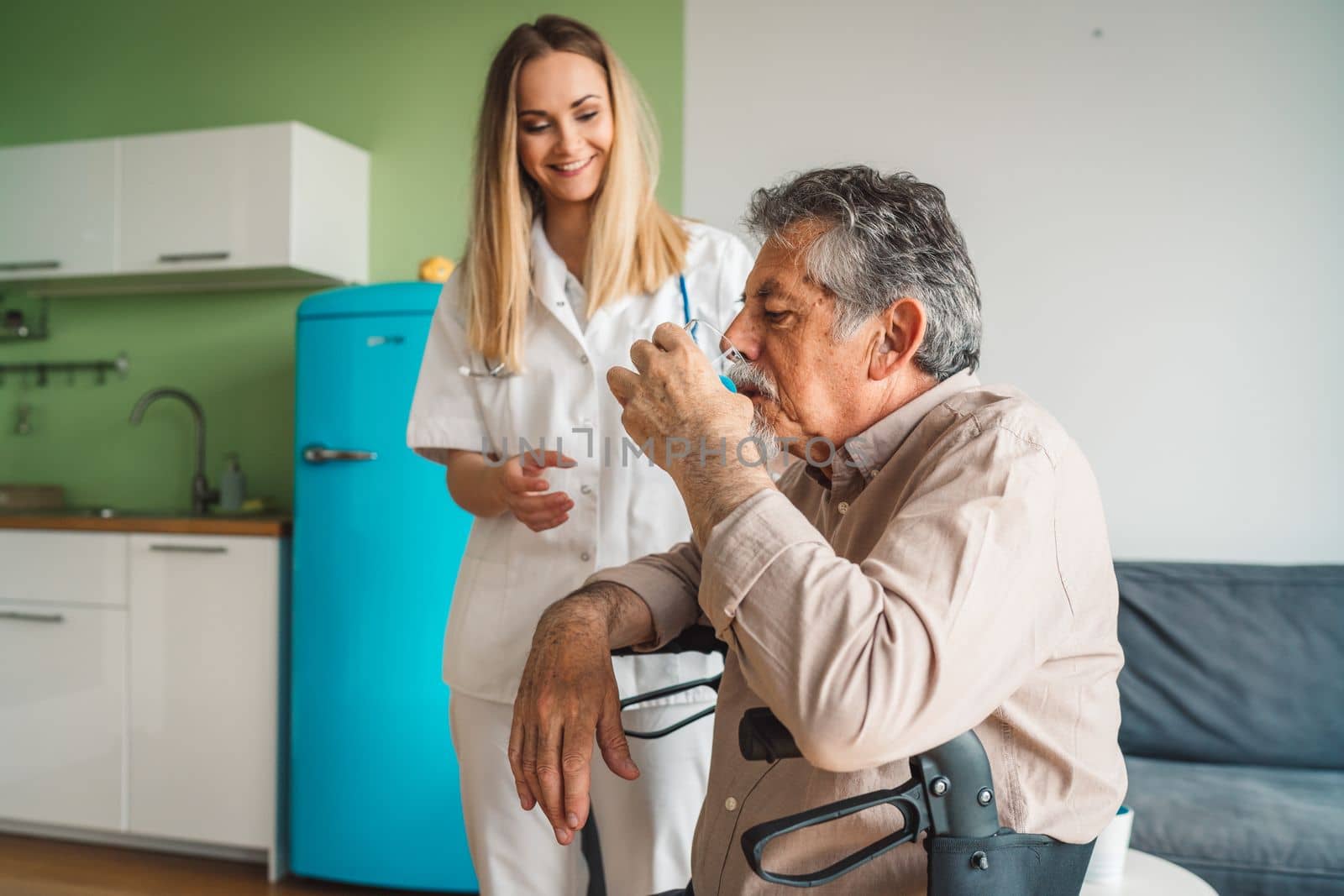 Young blonde woman caregiver helping senior man at home. Nurse assisting her old man patient at nursing home. Senior man being helped by nurse at home. High quality photo