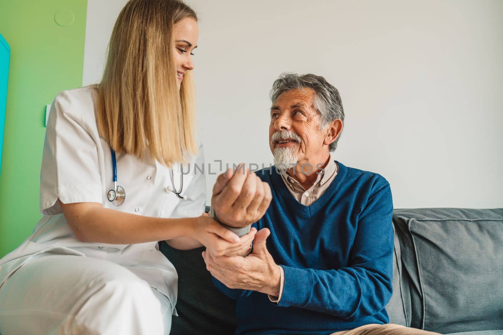 Young blonde woman caregiver helping senior man at home. Nurse assisting her old man patient at nursing home. Senior man being helped by nurse at home. High quality photo
