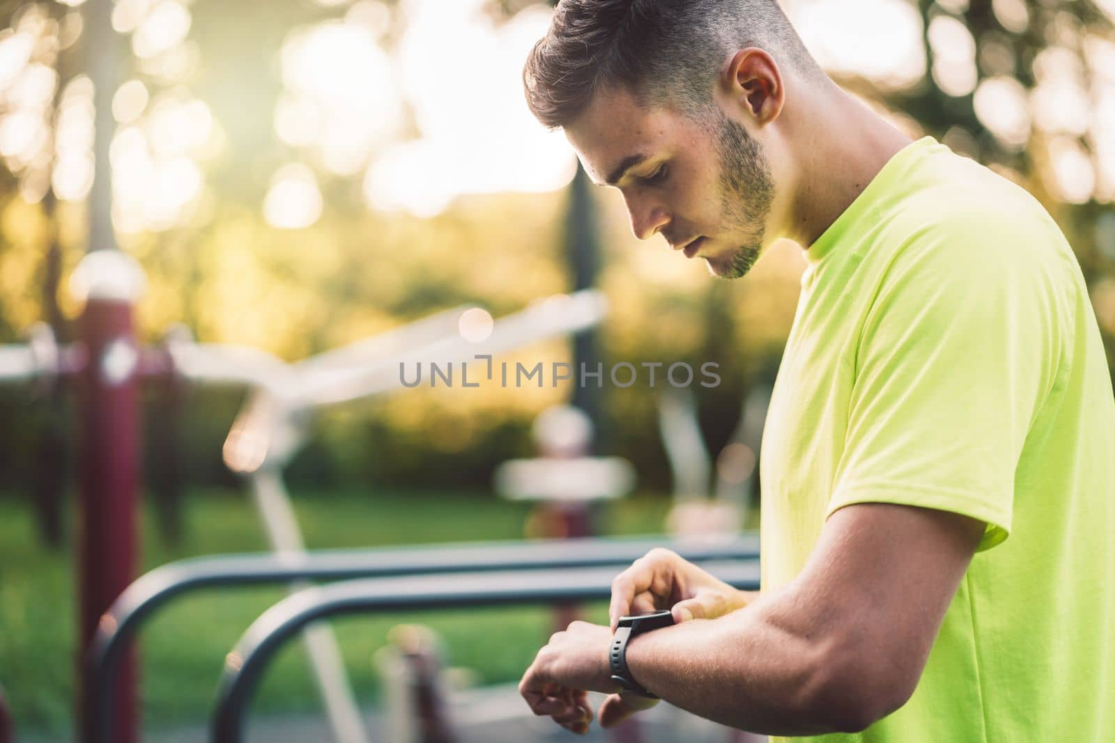 Caucasian man in green shir looking down at his watch, about to start running by VisualProductions