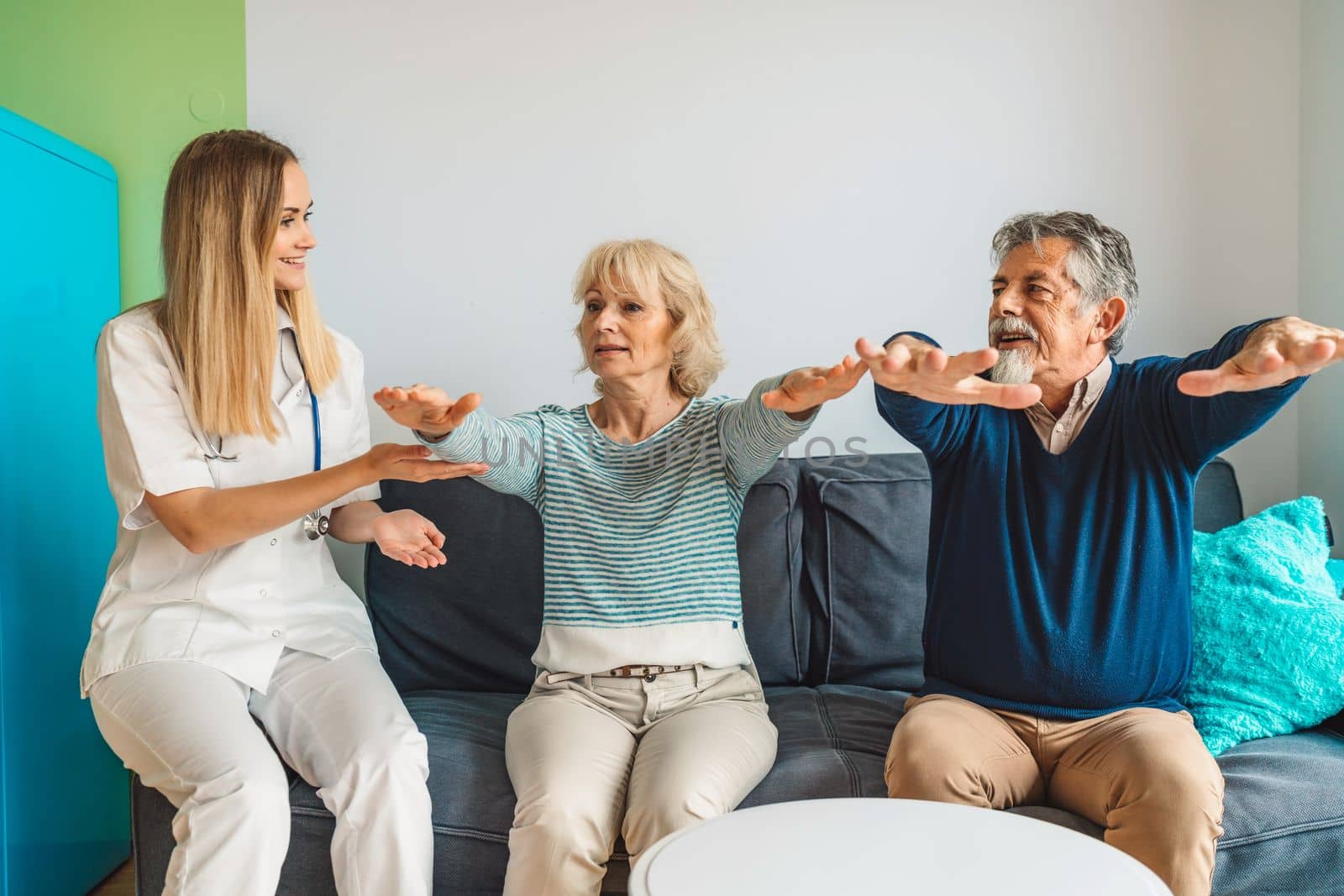 Woman caregiver assisting senior couple at nursing home, showing them some exercises by VisualProductions