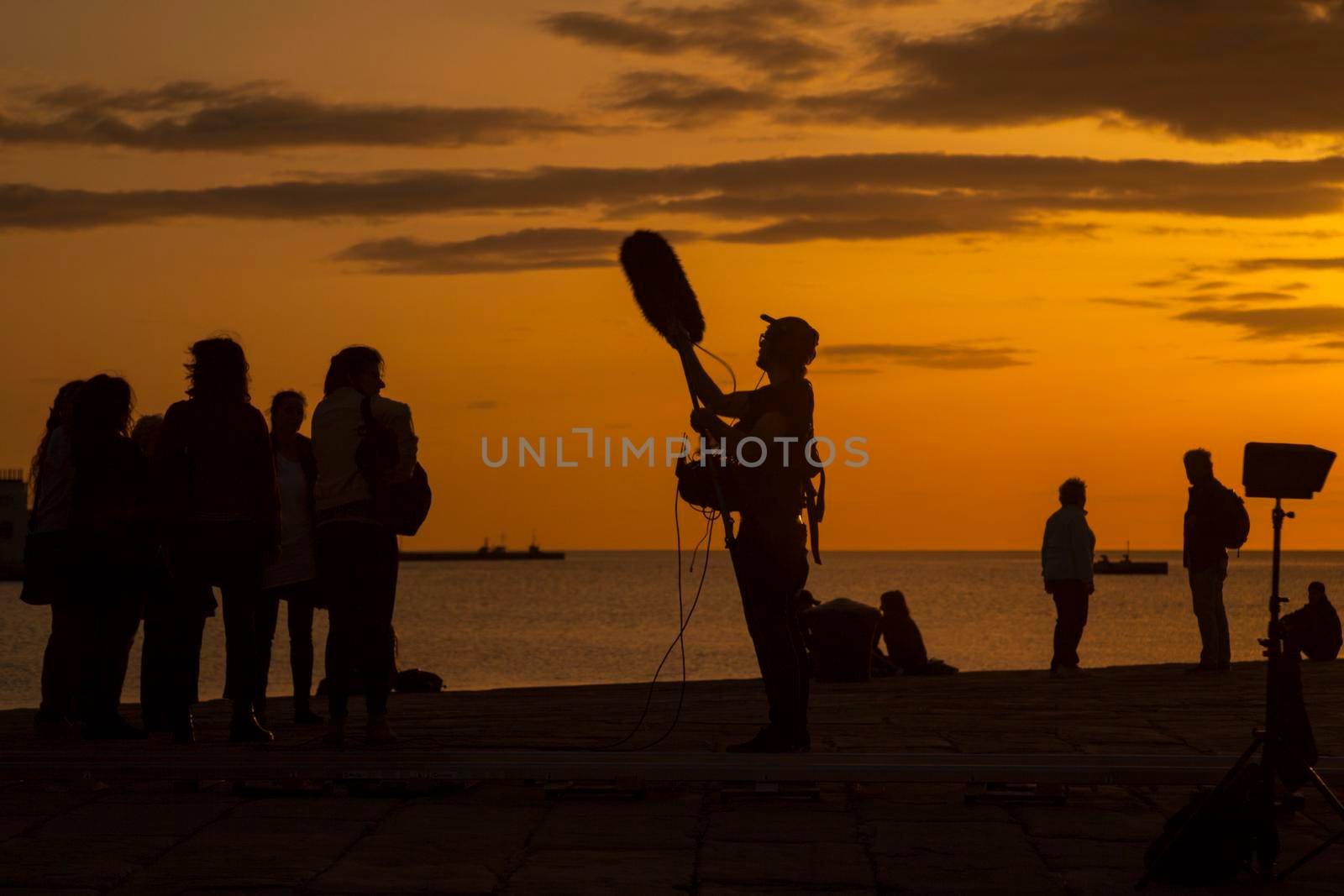 TRIESTE, ITALY - APRIL, 17: Behind the scene. Sound recorder with microphone, boom mic and headphones together the film crew team filming movie scene on outdoor location at sunset on April 17, 2018