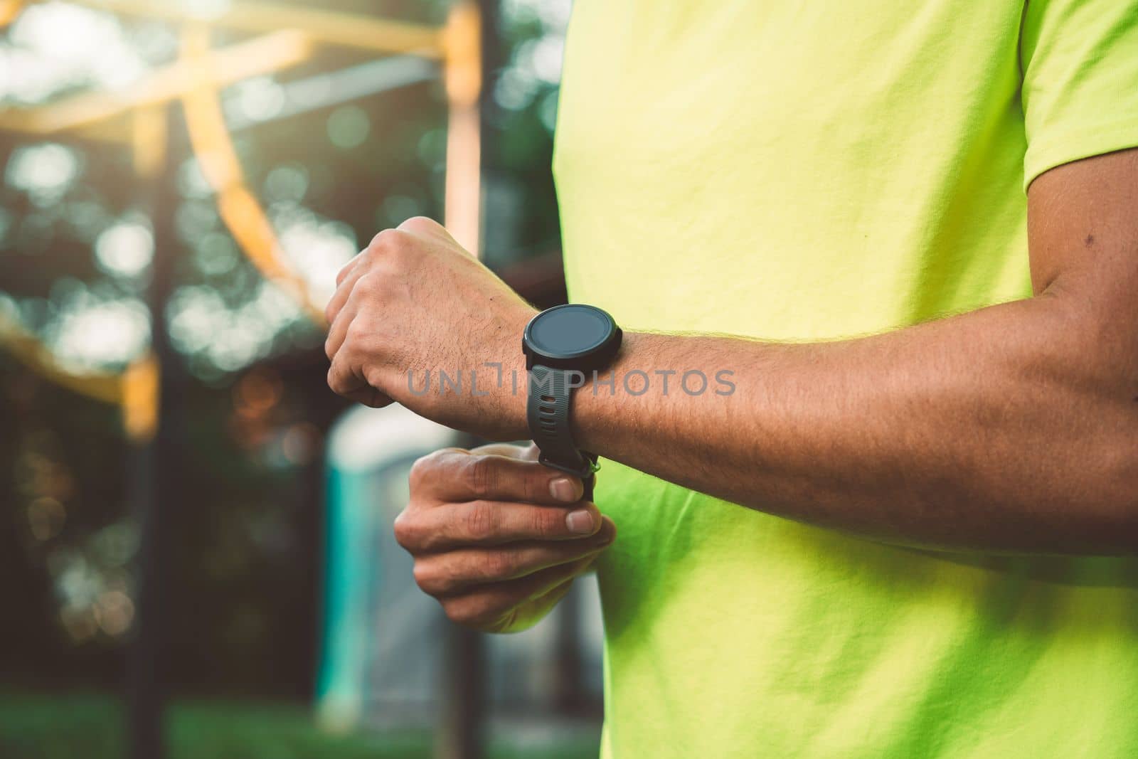 Fit man in green shirt wearing a sports watch during his run by VisualProductions