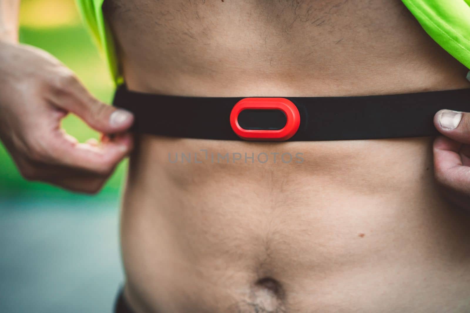 Unrecognizable man putting on the waist band to measure his pulse during a run by VisualProductions