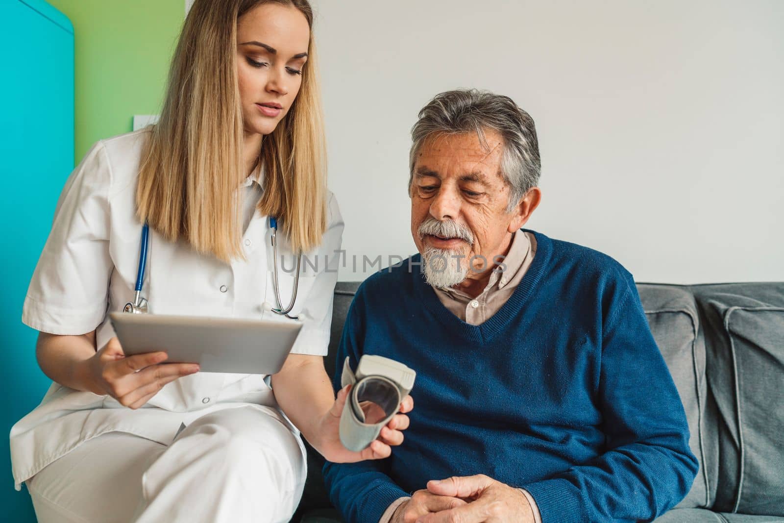 Young blonde woman caregiver helping senior man at home. Nurse assisting her old man patient at nursing home. Senior man being helped by nurse at home. High quality photo
