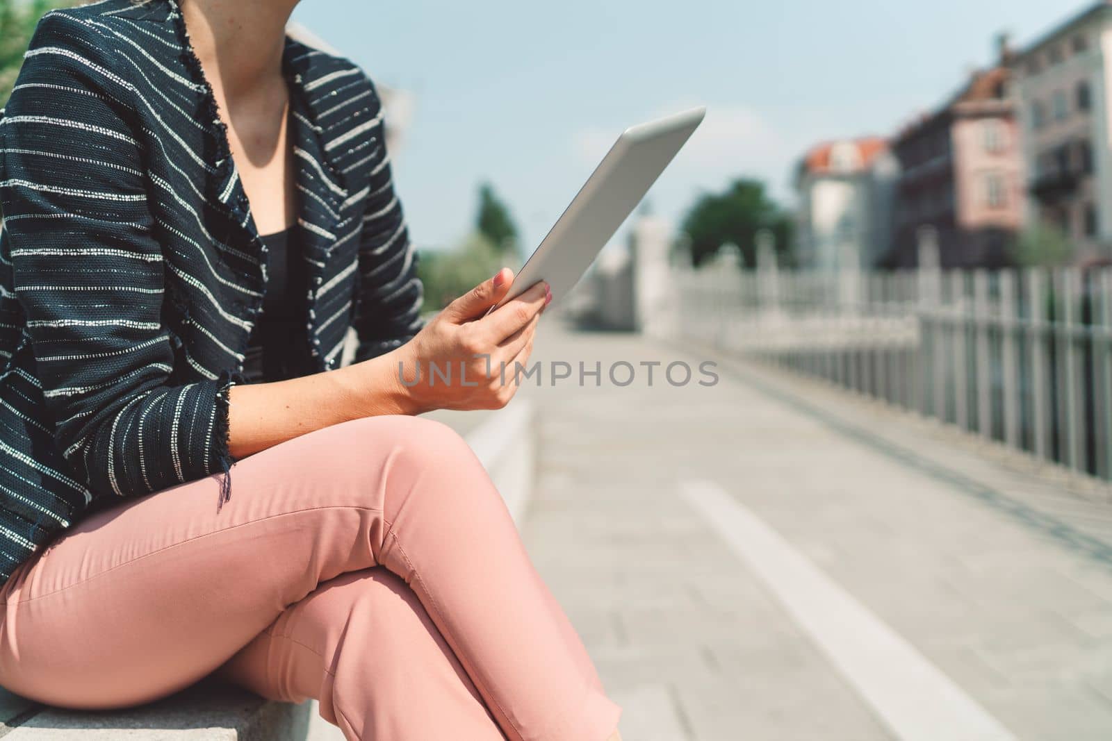Unrecognizable woman sitting on the sun with crossed legs holding a digital tablet in his hands by VisualProductions