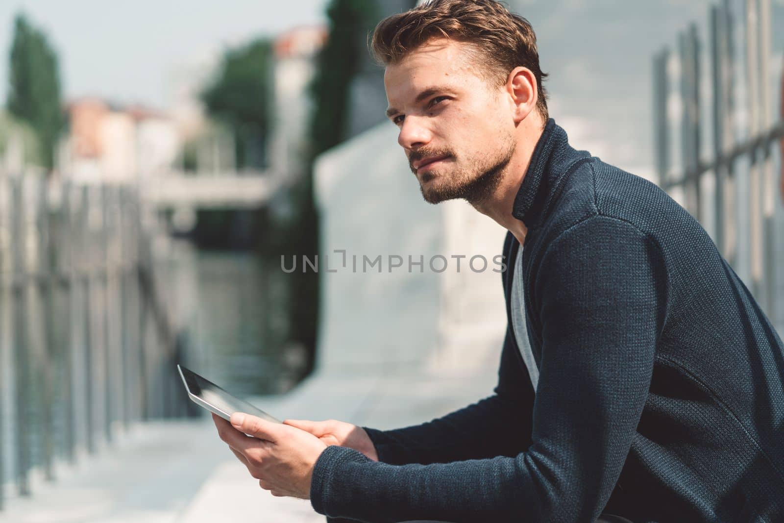 Serious looking man sitting on the sun with phone in his hands by VisualProductions
