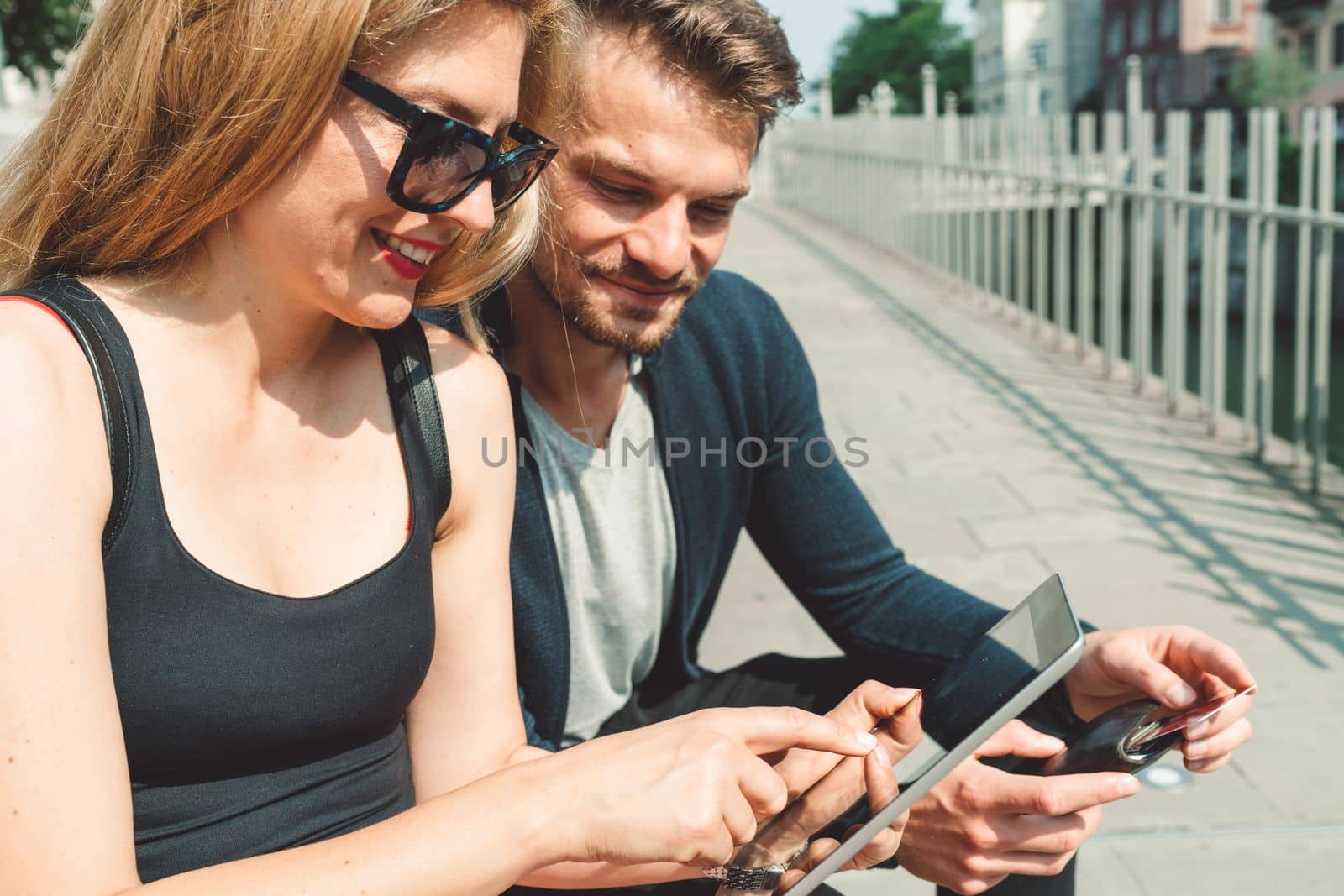 Young woman looking at the tablet while her boyfriend leans in to see what she is watching - City life by VisualProductions