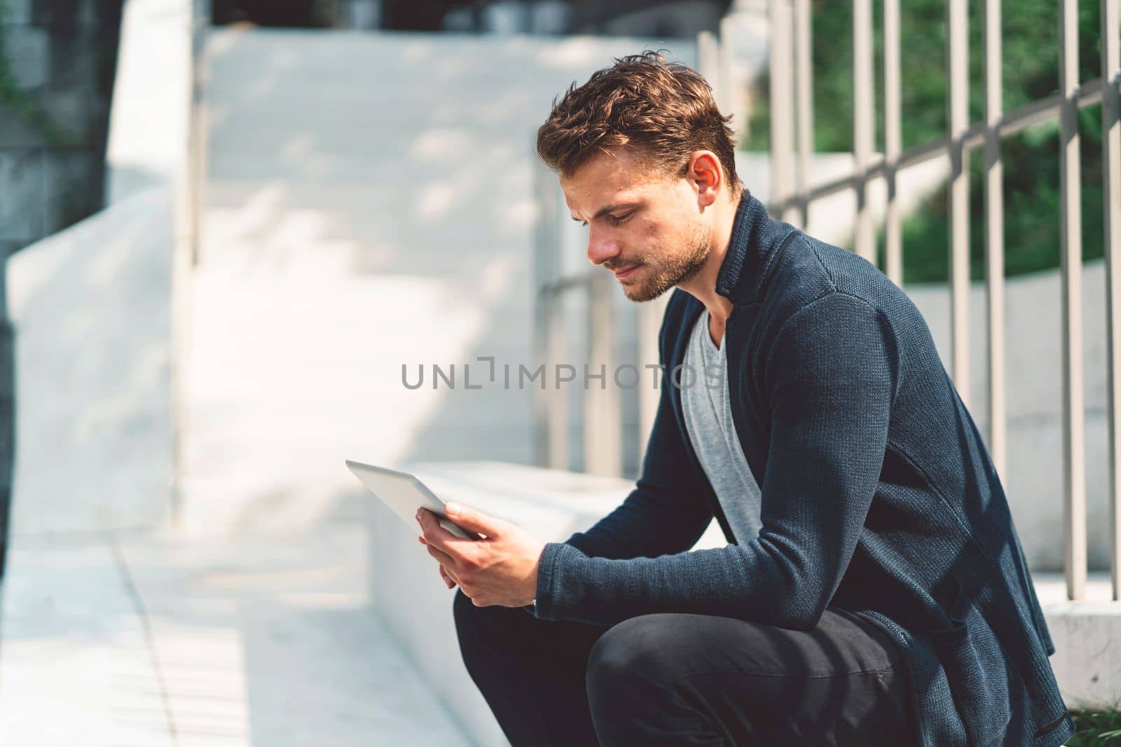 Caucasian man working on the tablet during his lunch break, sitting outside in the sun by VisualProductions