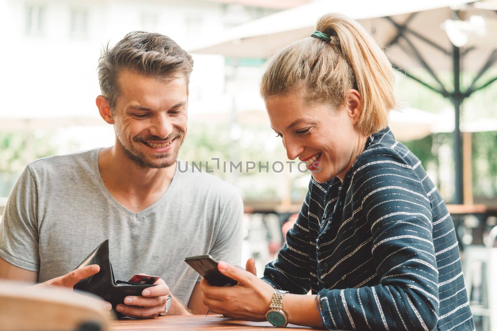 Young couple smiling while looking at their phone, sitting at a bar waiting for their drinks by VisualProductions