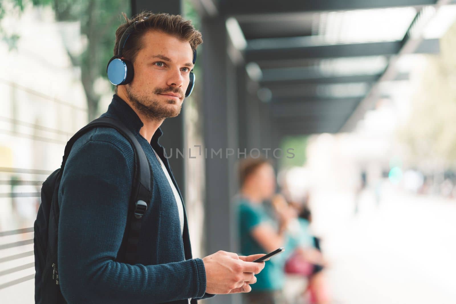 Wait up man with headphones listening to music at the bus station by VisualProductions