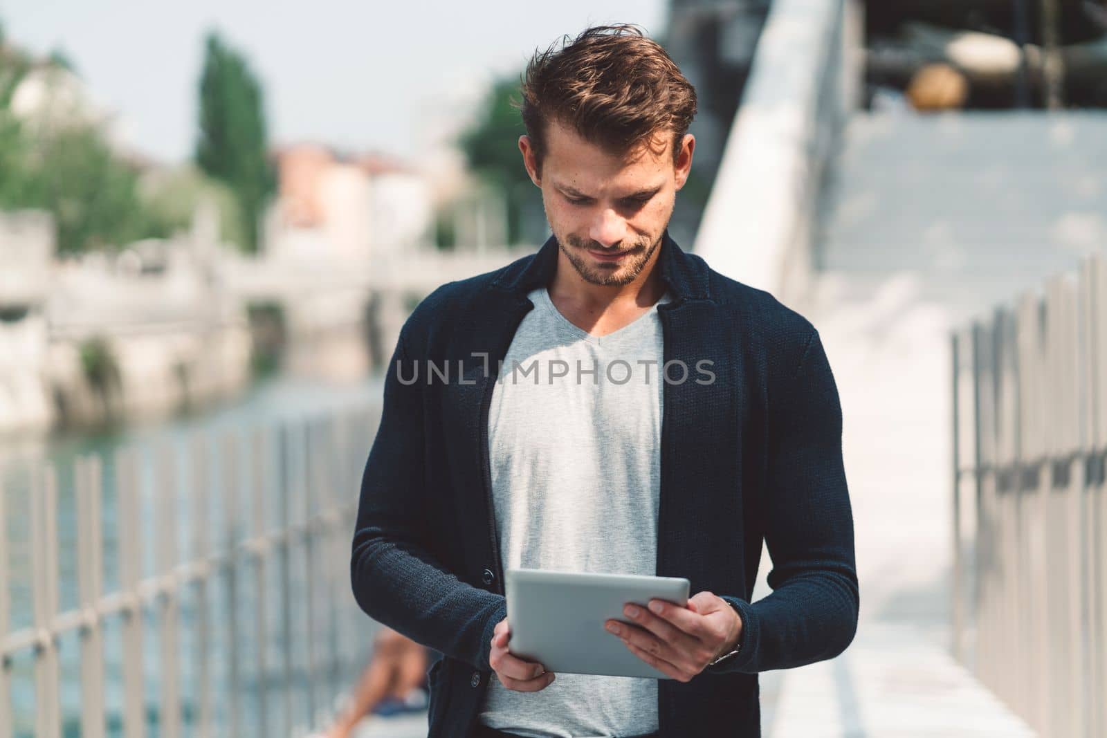 Profile of young man looking down at the digital tablet in his hands, while walking around the city by VisualProductions