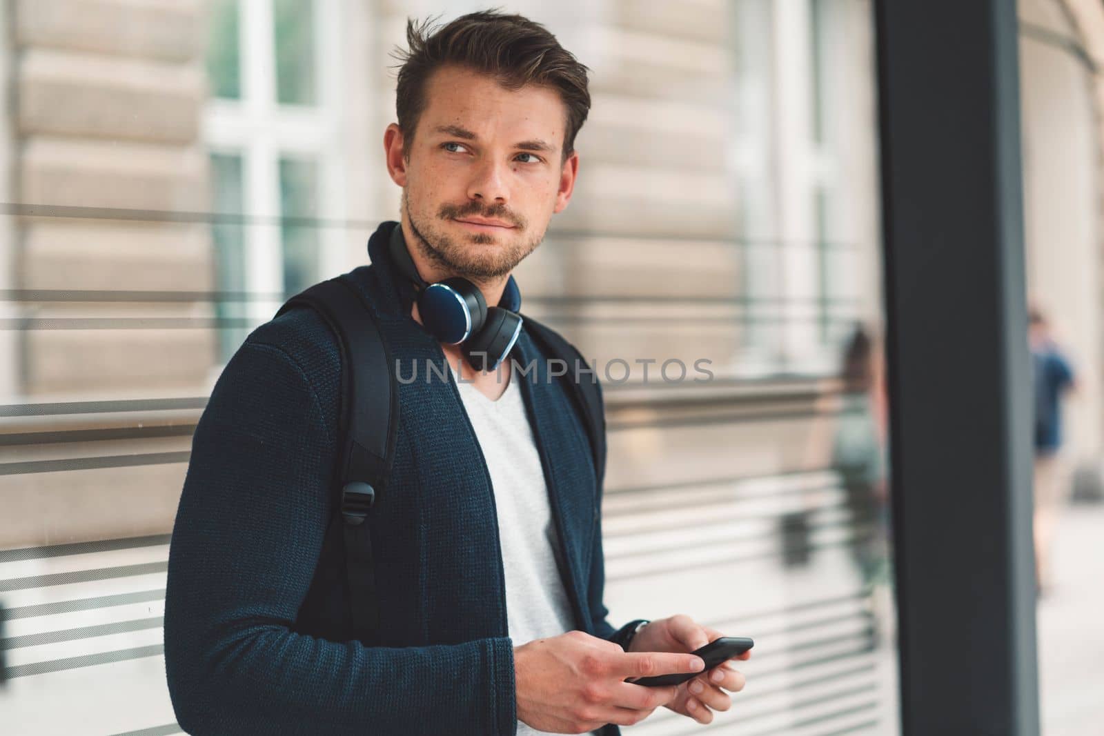 Waist up caucasian man with headphones around his neck, waiting at the bus station by VisualProductions
