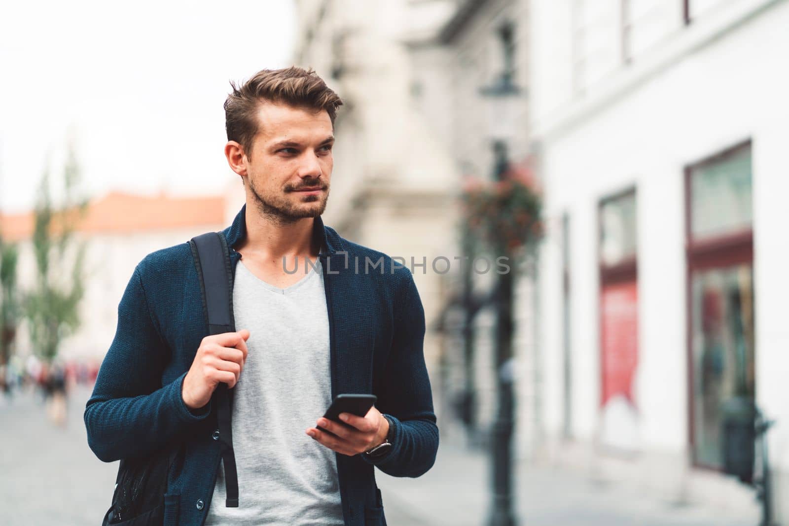 Wait up portrait of caucasian bearded man walking around the city with a phone in his hands by VisualProductions