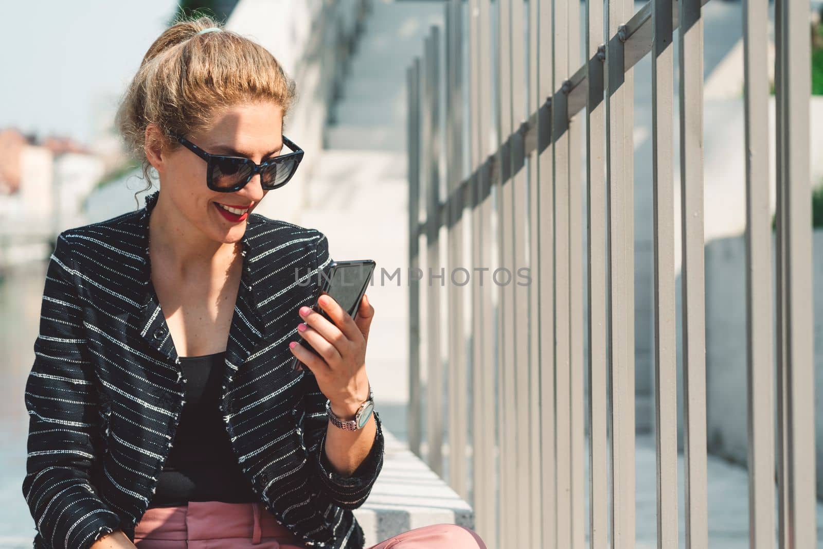 Woman with her hair in a ponytail looking at the phone while on a lunch break outside by VisualProductions