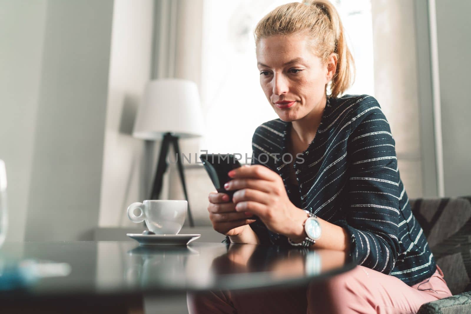 Young londe woman sitting at a cafe looking at her phone by VisualProductions