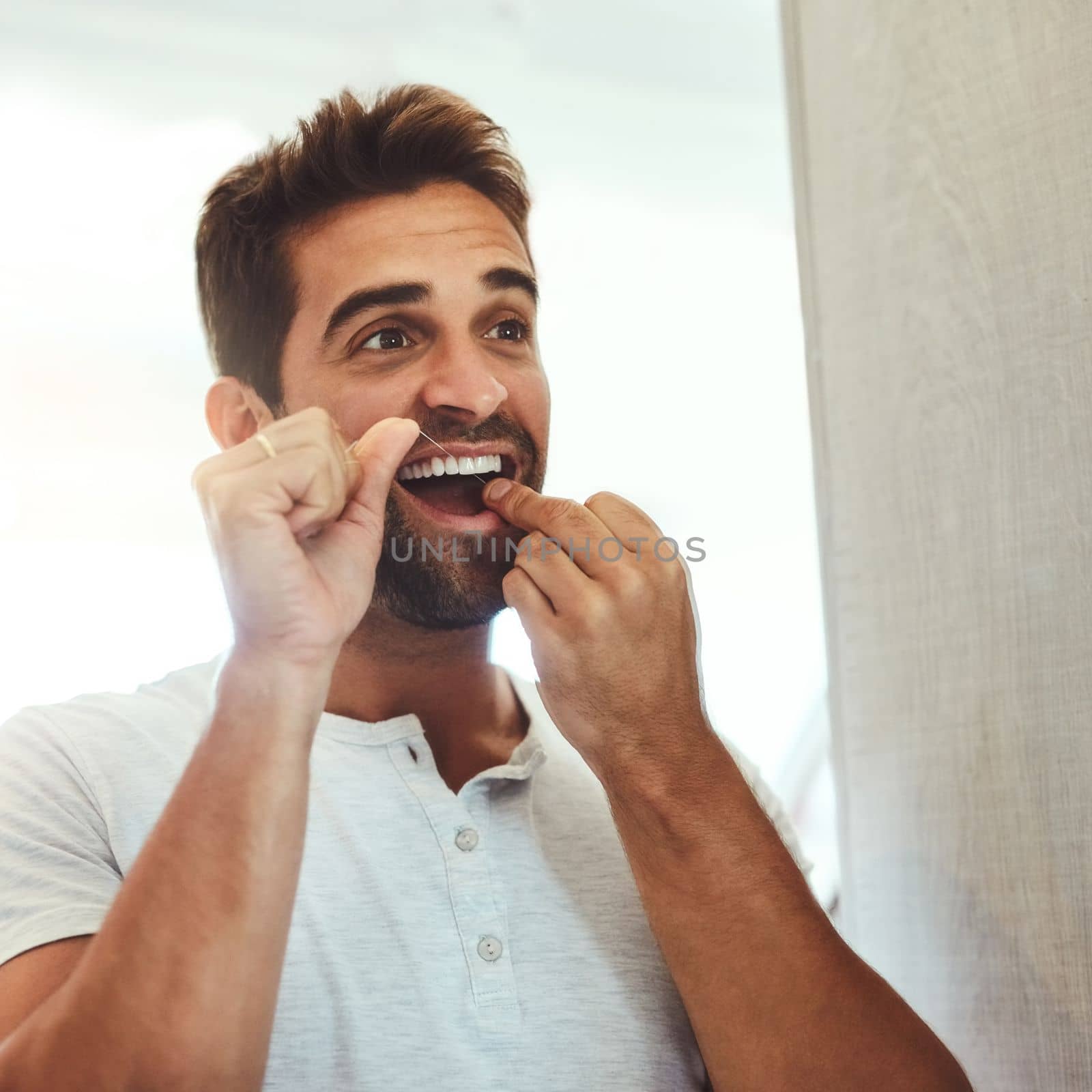 Got to look my best. a handsome young man flossing his teeth while looking at his reflection in the mirror at home. by YuriArcurs