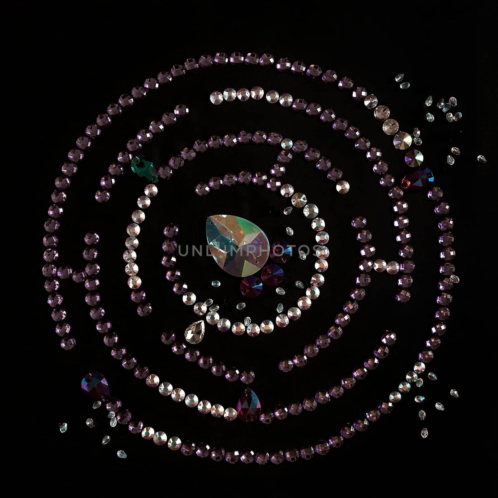 Rhinestones in the form of a labyrinth with a flat lay, isolated on a black background. Top view pattern or labyrinth of rhinestones in lilac and silver color