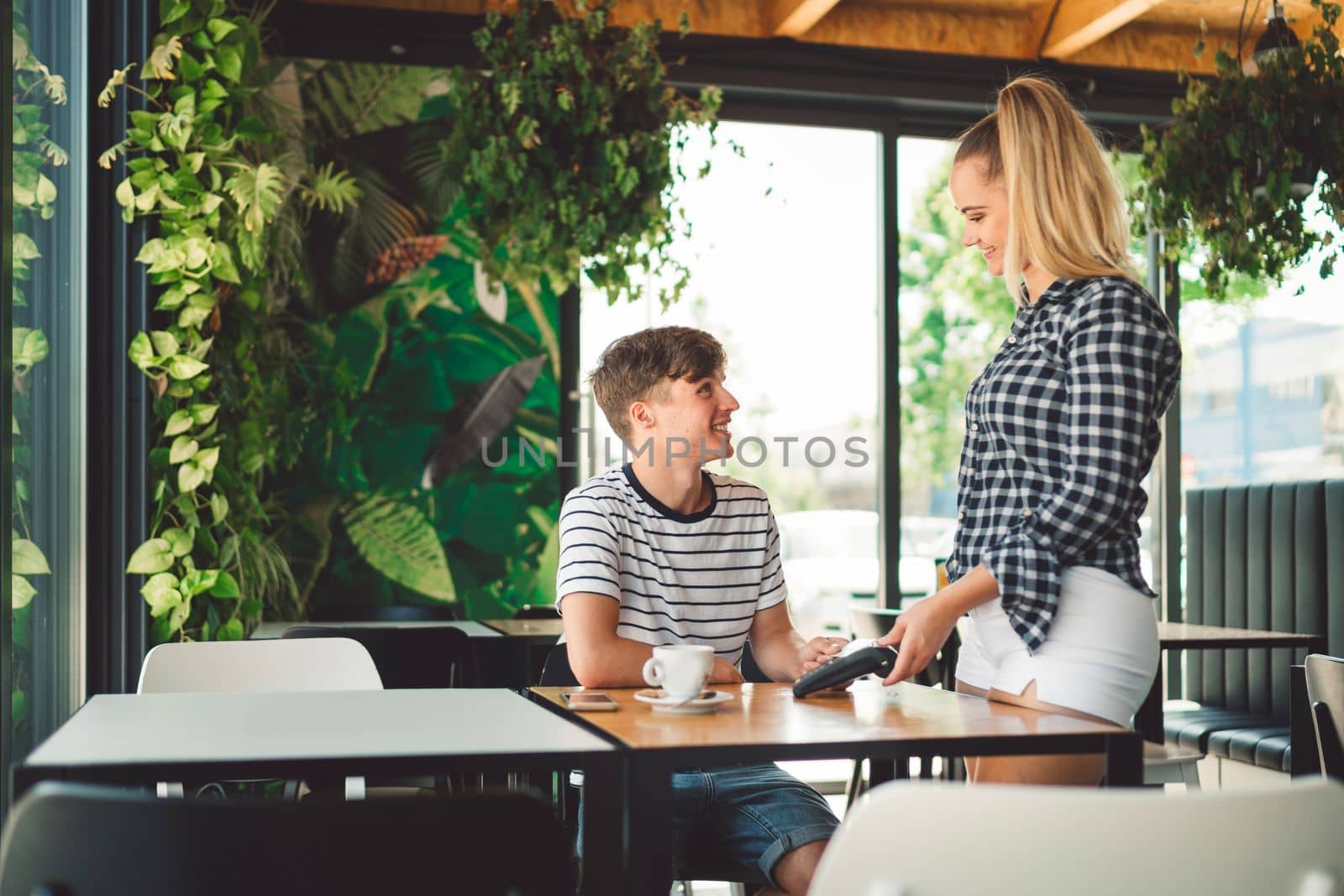 Young caucasian person using a wireless payment method. Young person holding her credit card next to a card reader, paying for her coffee.