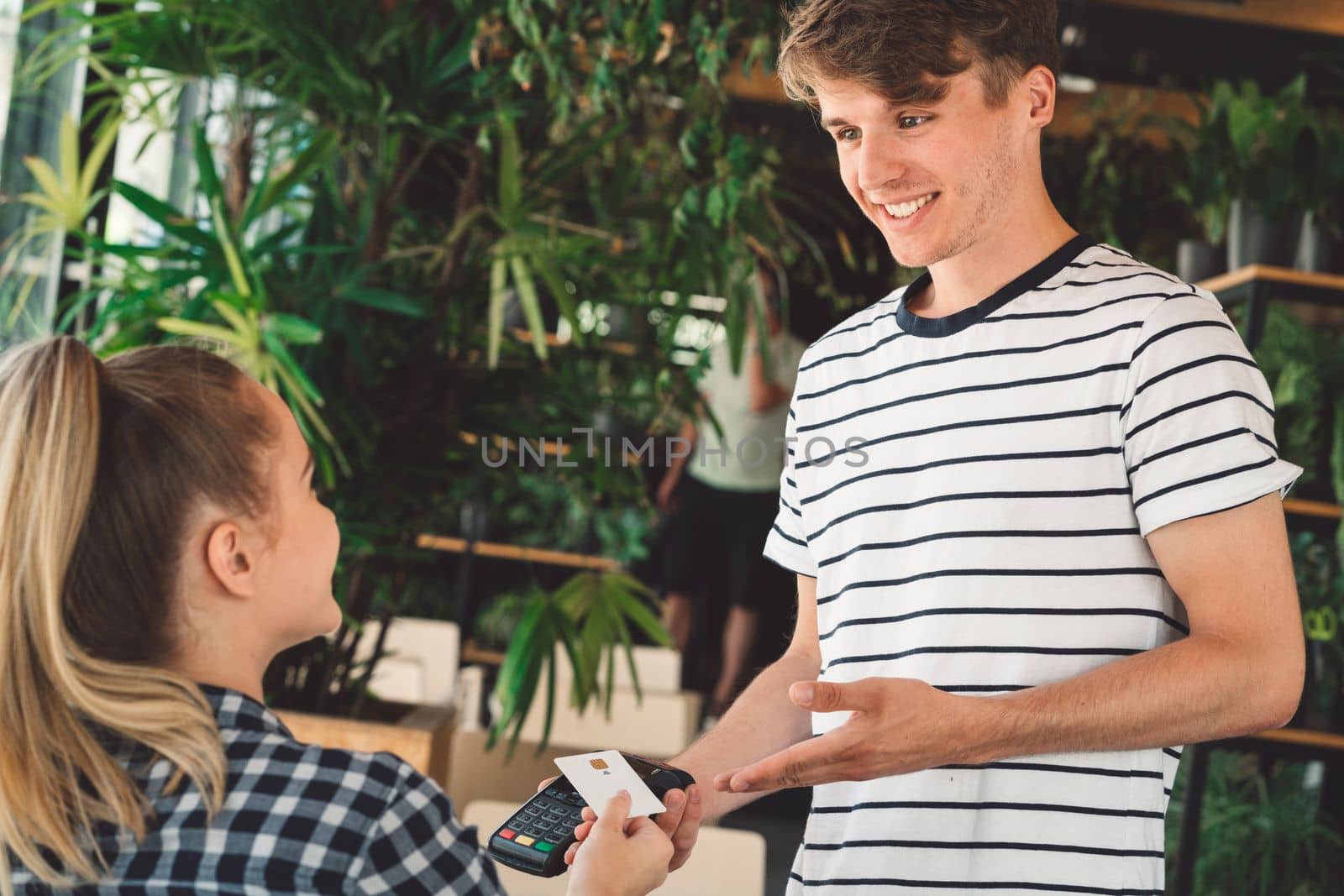 Young caucasian person using a wireless payment method. Young person holding her credit card next to a card reader, paying for her coffee.