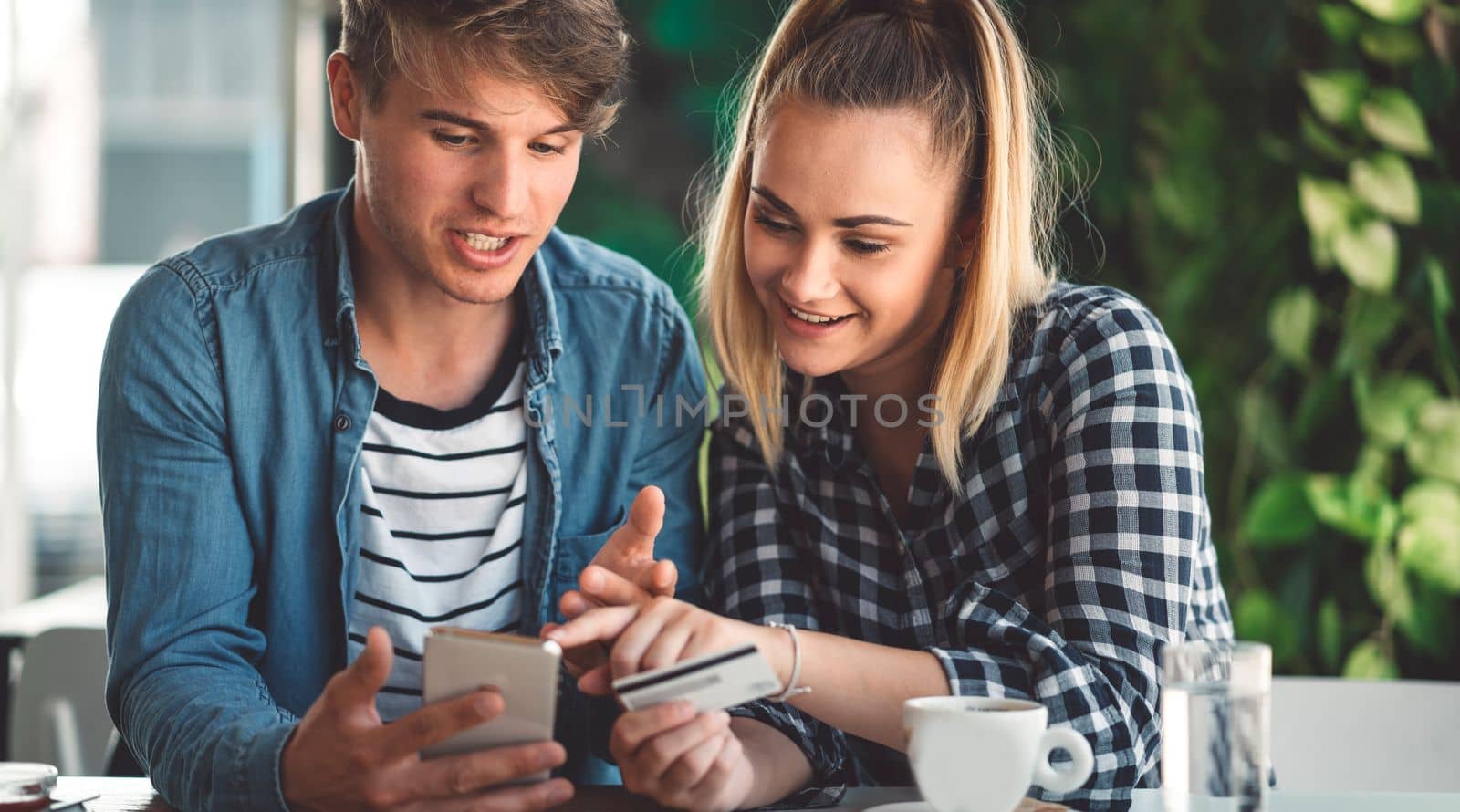 Young caucasian couple of students sitting at a cafe online shopping on their laptop. Both smiling while looking at the laptop.