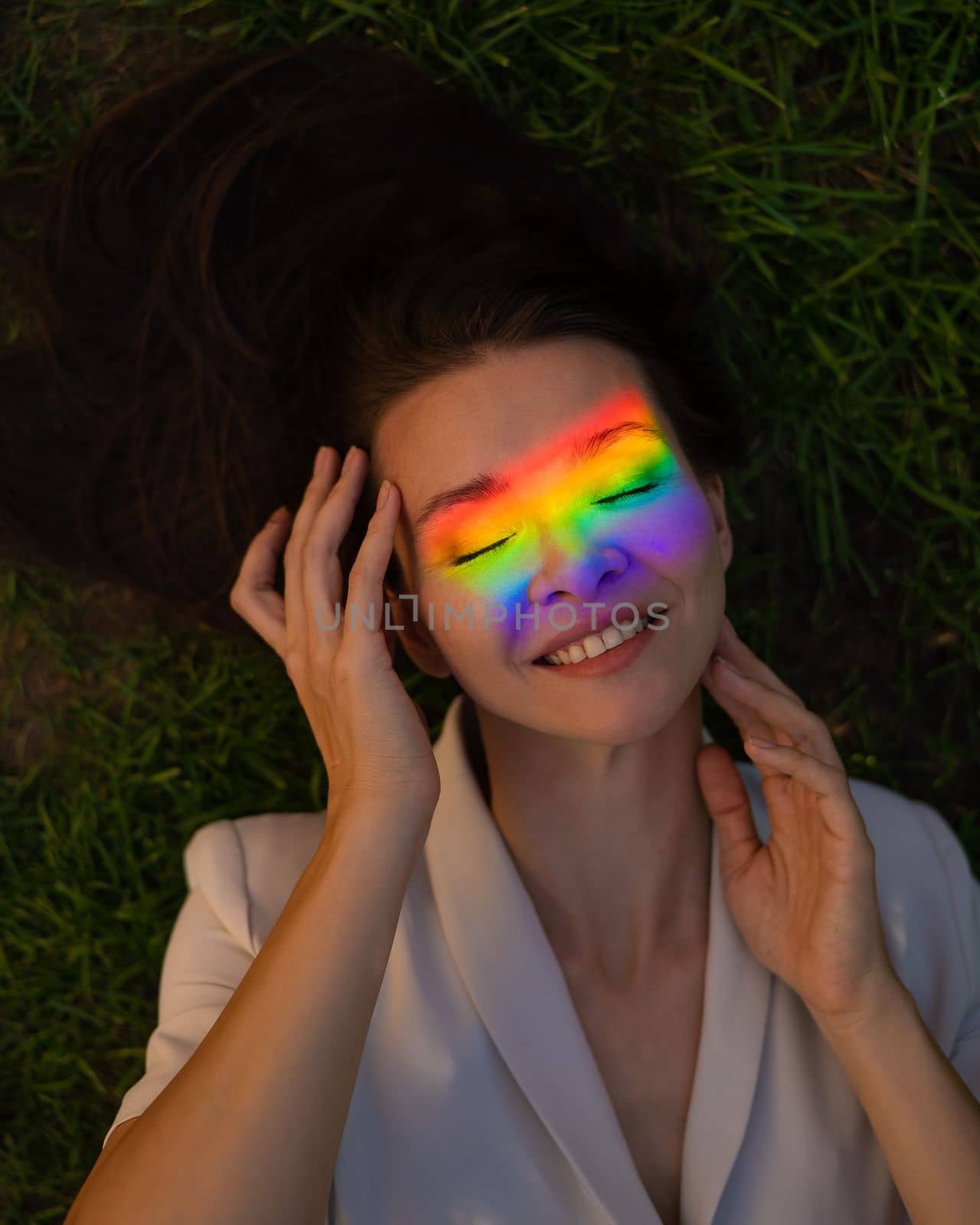 Top view of caucasian woman with rainbow ray on her face lies on green grass