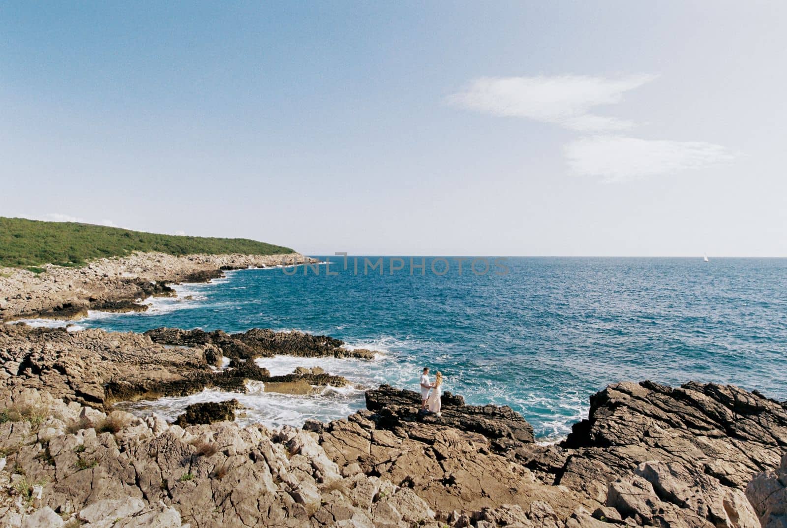 Man and woman stand on rocks holding hands near blue water. High quality photo