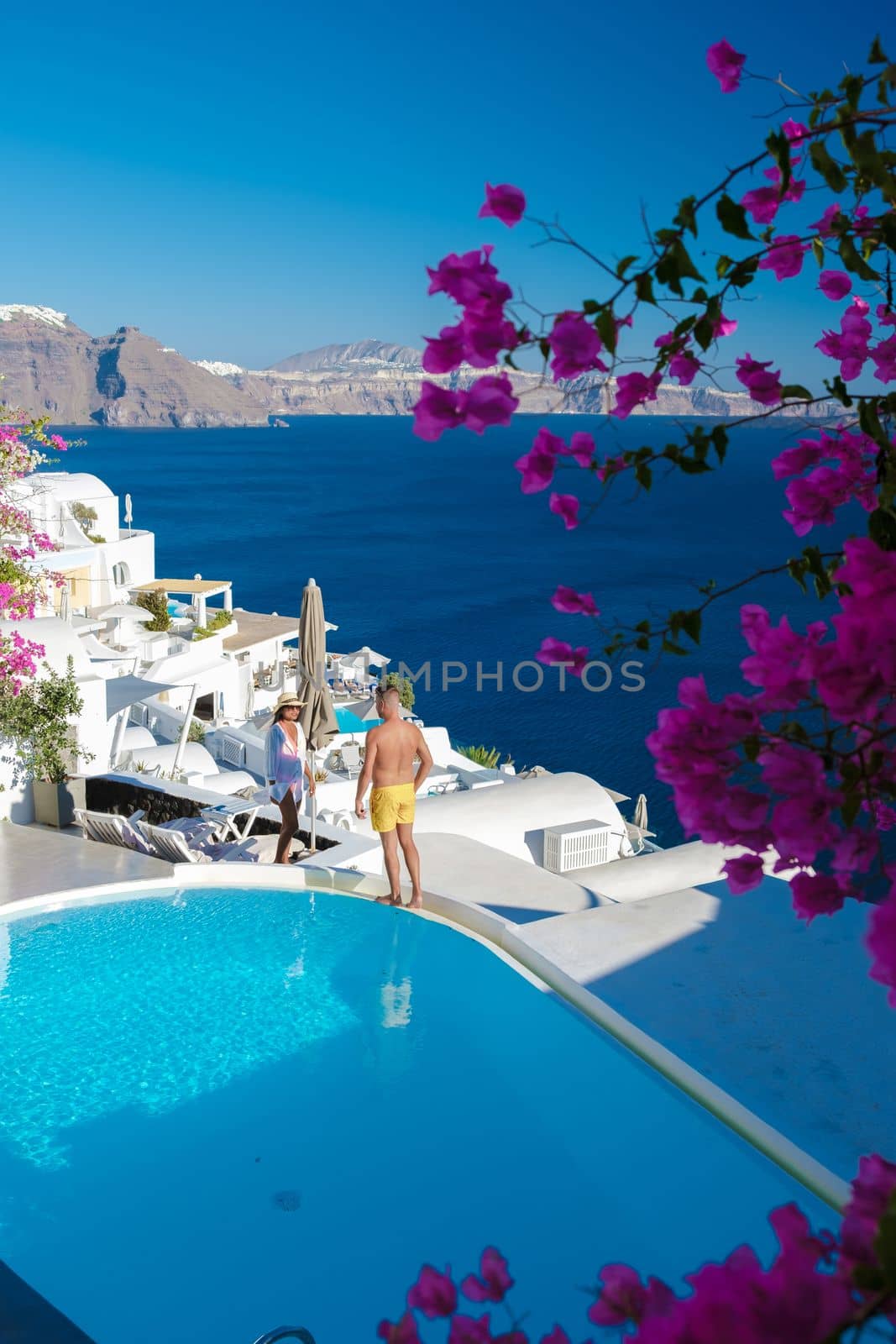 Couple on vacation in Greece, men and women relaxing by a swimming pool of a luxury resort during summer vacation