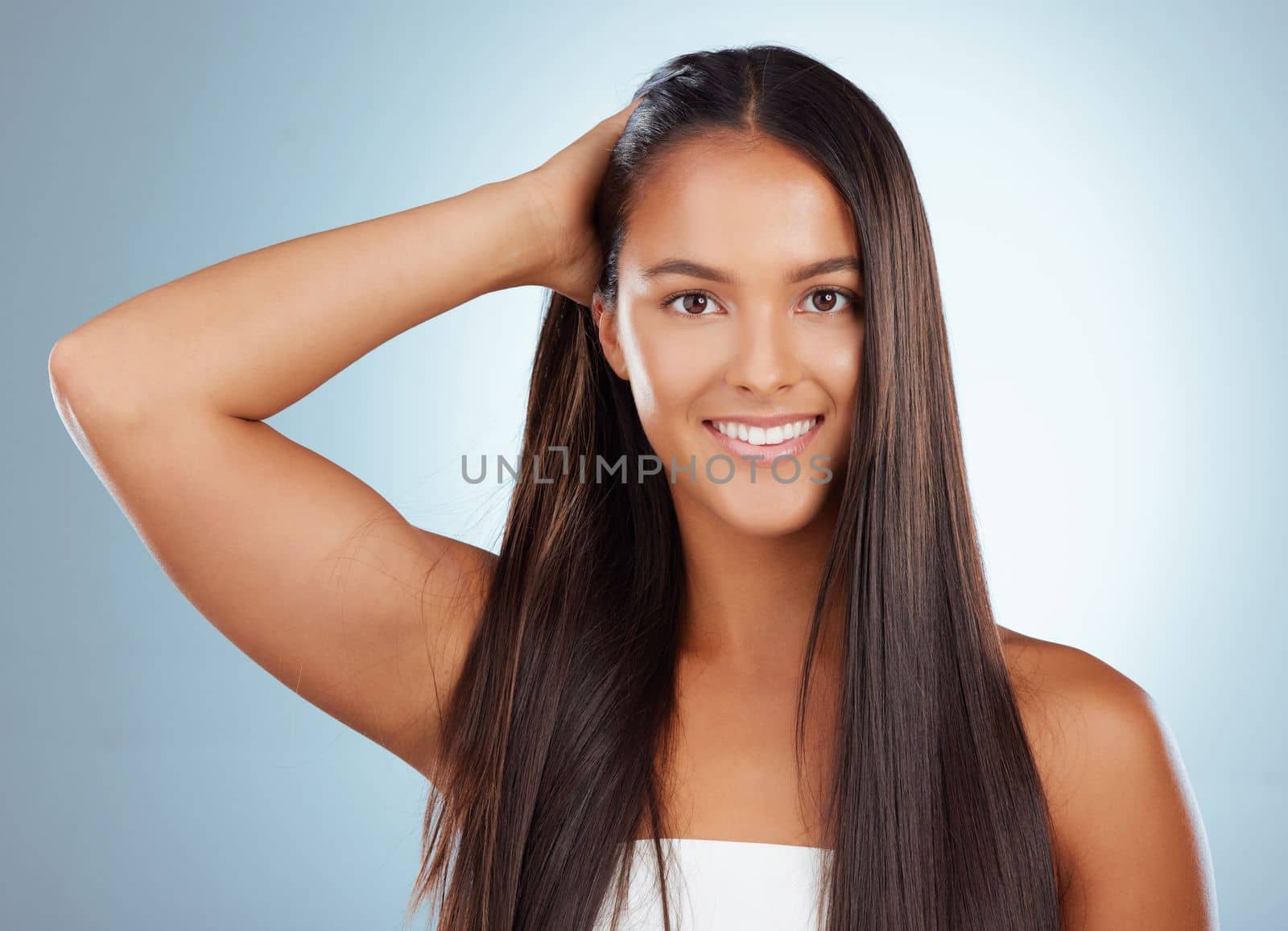 Portrait of a hispanic brunette woman with long lush beautiful hair smiling and posing against a grey studio background. Mixed race female standing showing her beautiful healthy hair.