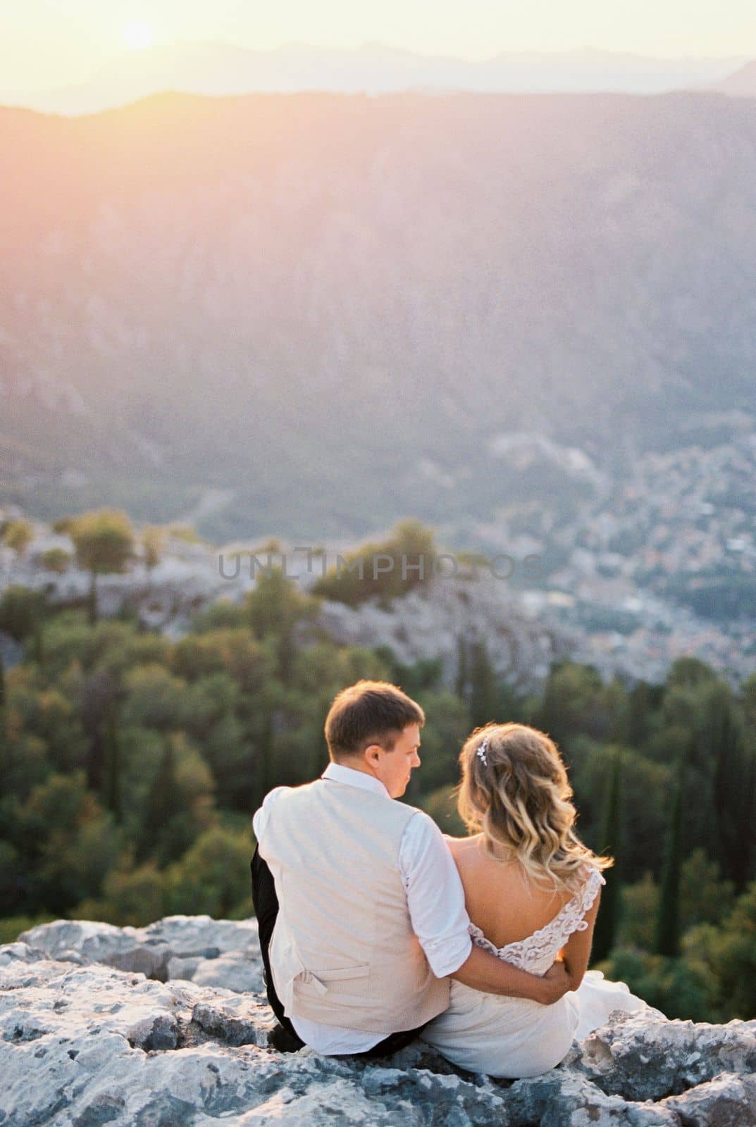 Bride and groom are sitting on the top of the mountain and looking at the valley. High quality photo