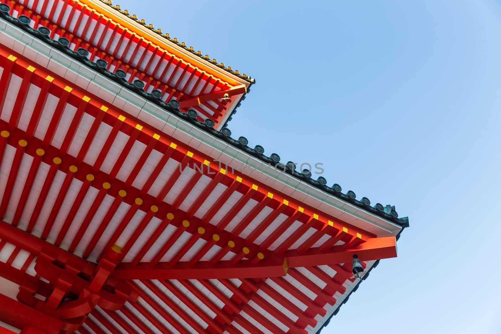 Under the classic japanese red roof with bright blue sky in background.