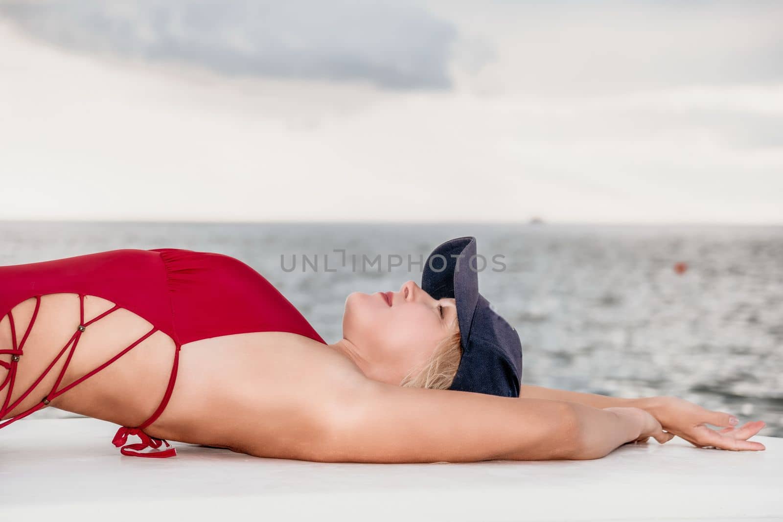Woman in red bikini on Beach. Happy lady with blond hair in bathing suit chilling and sunbathing by turquoise sea ocean on sunset. Holiday, vacation and recreational concept. Close up by panophotograph