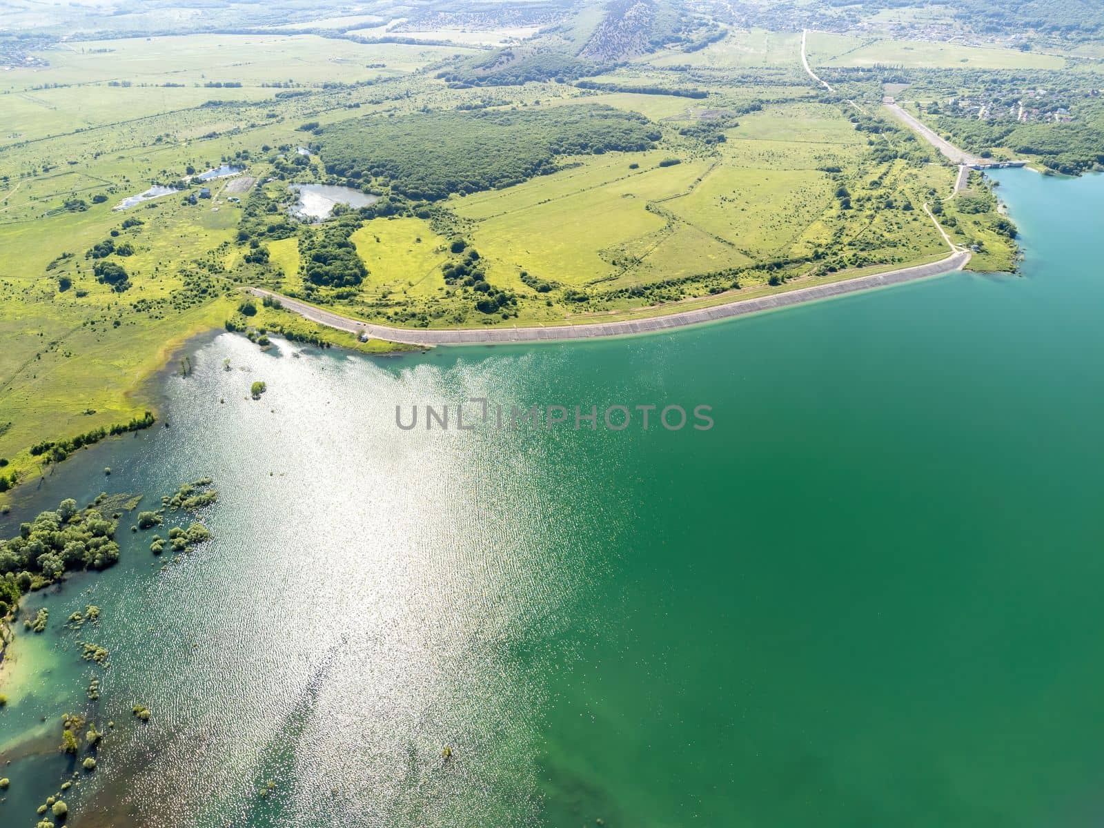Aerial landscape from flying drone storage reservoir at mountain foot covered colorful spring forest. Beautiful view from above blue lake among highlands