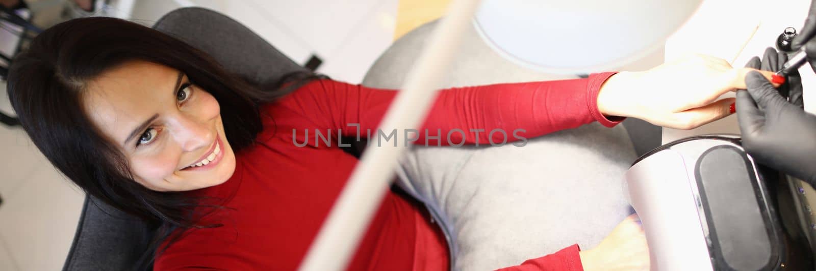 Portrait of beautiful young brunette woman doing red manicure in nail salon. Care of nails and skin of hands concept