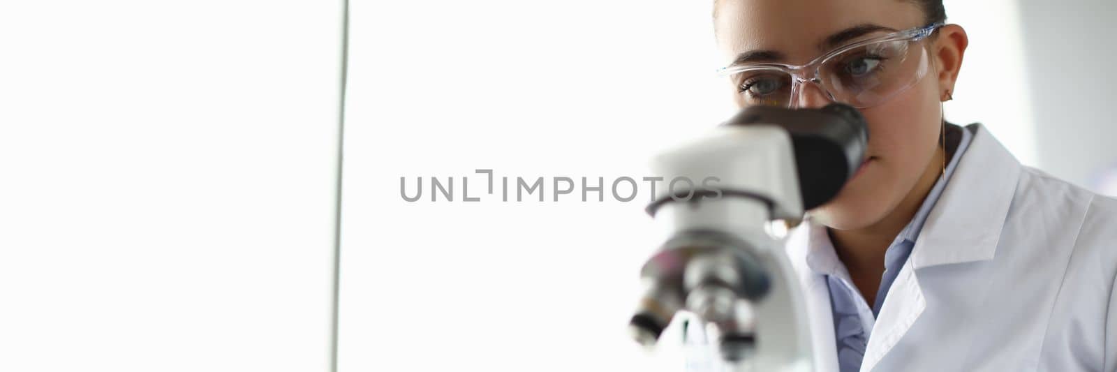 Young woman scientist looks into microscope. Doctor using microscope in laboratory examines tests