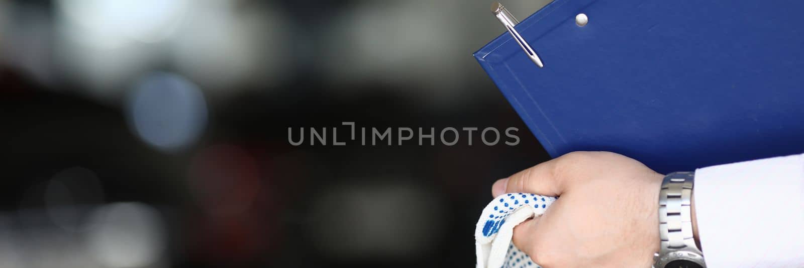 Car mechanic priemchik holds gloves and clipboard in car service by kuprevich