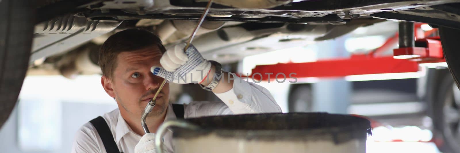 Auto mechanic checks running gear of car and oil leak at service station by kuprevich